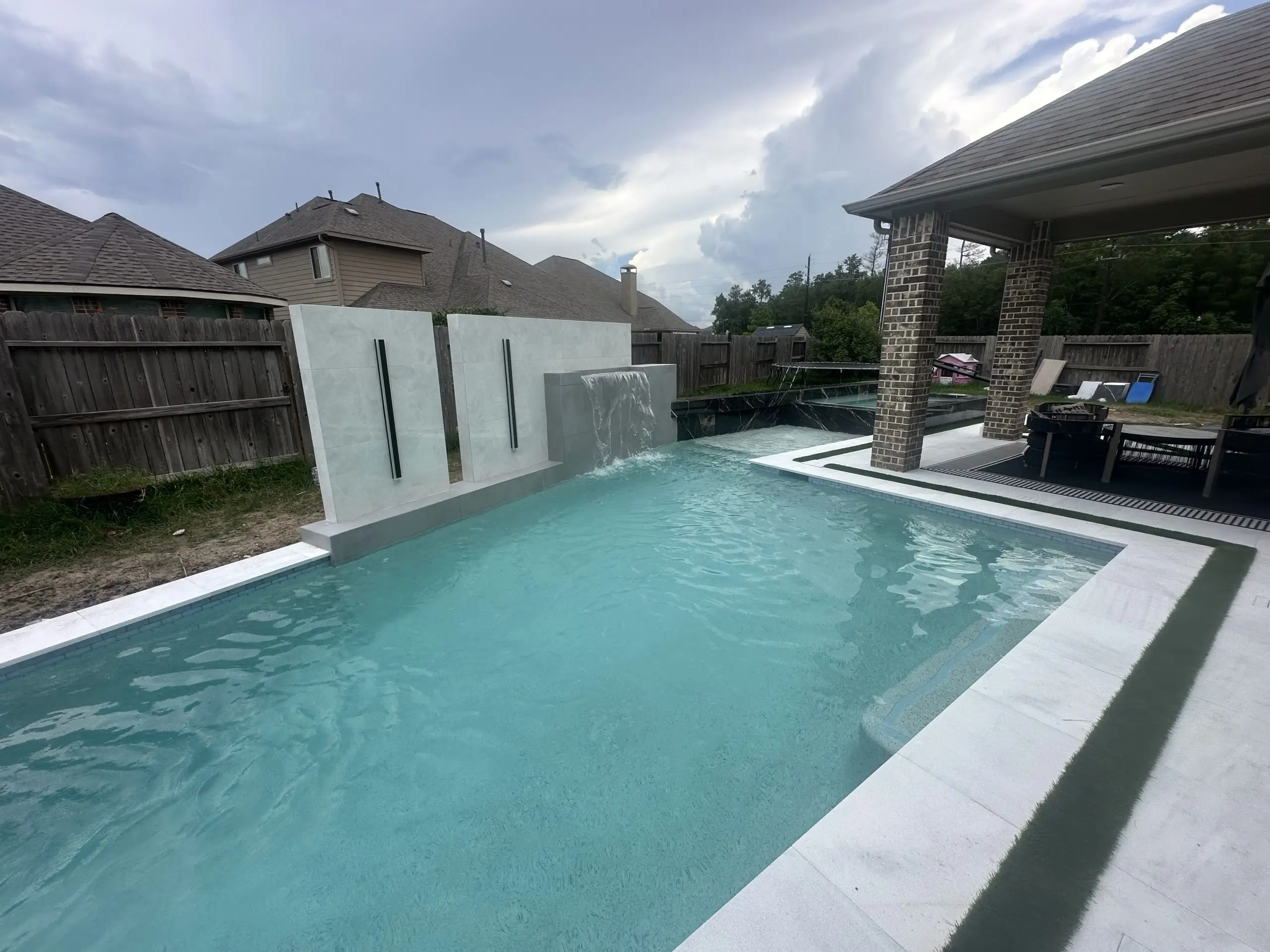 Modern backyard pool featuring a raised water wall with vertical LED lights, sheer descent waterfall, and attached covered patio.